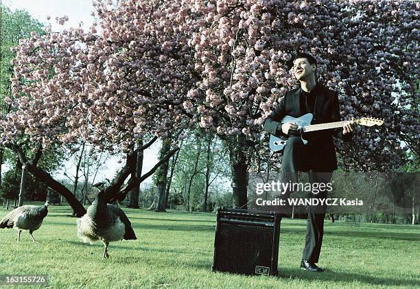 Rendezvous With Etienne Daho. Attitude d'Etienne DAHO jouant de sa guitare électrique, un pied posé sur l'amplificateur, dans un parc avec un arbre...