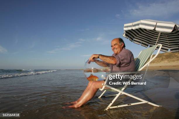 Island Of Re And Celebrities. Attitude souriante de Jean BENGUIGUI assis les pieds dans l'eau, son poisson rouge Niki dans un bocal, sur la plage du...