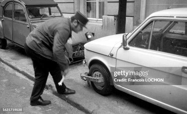 Un policier pose un sabot de Denver sur une roue de voiture en novembre 1975 à Paris.