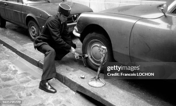 Un policier pose un sabot de Denver sur une roue de voiture en novembre 1975 à Paris.