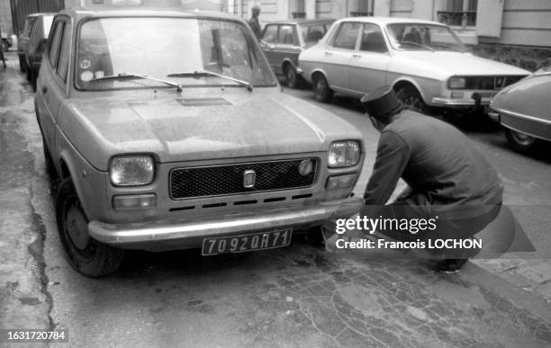 Un policier pose un sabot de Denver sur une roue de voiture en novembre 1975 à Paris.