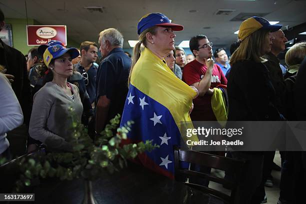 Marisa Perez is wrapped in a Venezuelan flag as she and others listen to what is being said on a television set reporting on the death of Venezuelan...