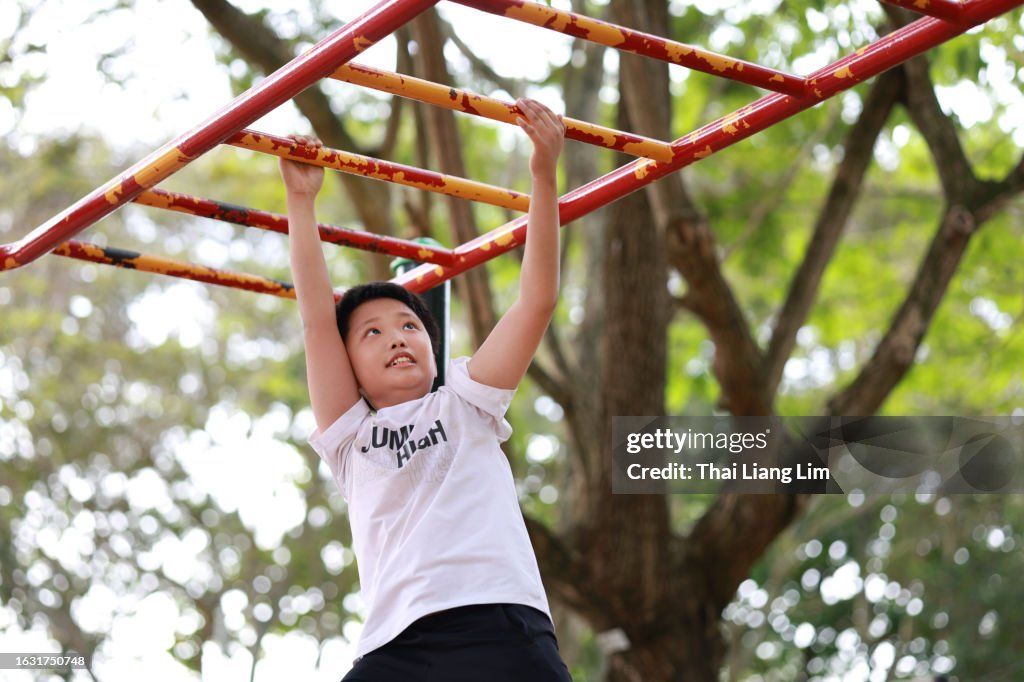 A lively Asian boy confidently navigating the monkey bars at a playground, demonstrating his physical agility and adventurous spirit.