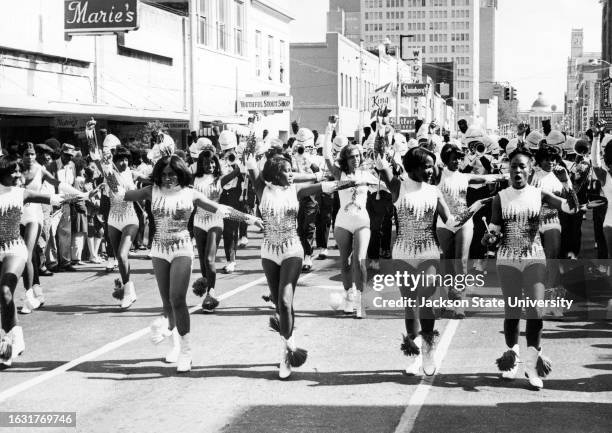 Female university students performing with band during Homecoming procession on street.