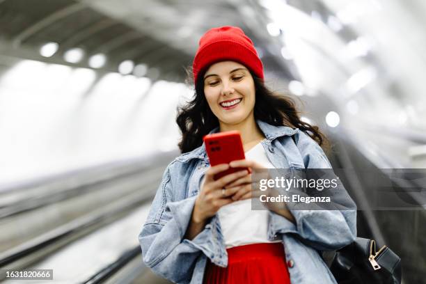 beautiful woman standing on escalator on her way to modern brightly lit subway station. public transportation and urban life concept. low angle shot. - travel stock pictures, royalty-free photos & images