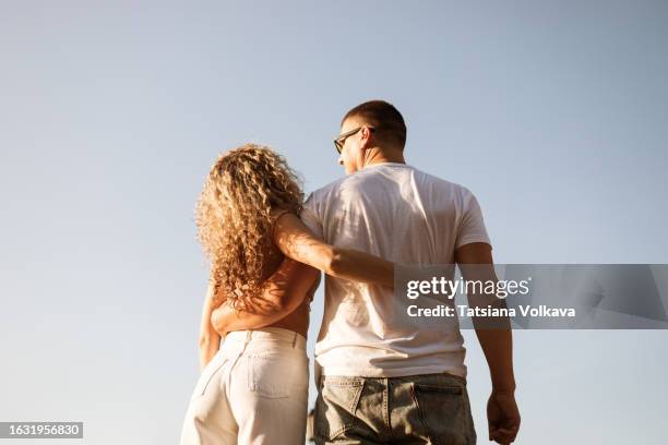 rear view of tall mature man and slender woman with curly hair standing with their hands on each other sides - innamorarsi foto e immagini stock