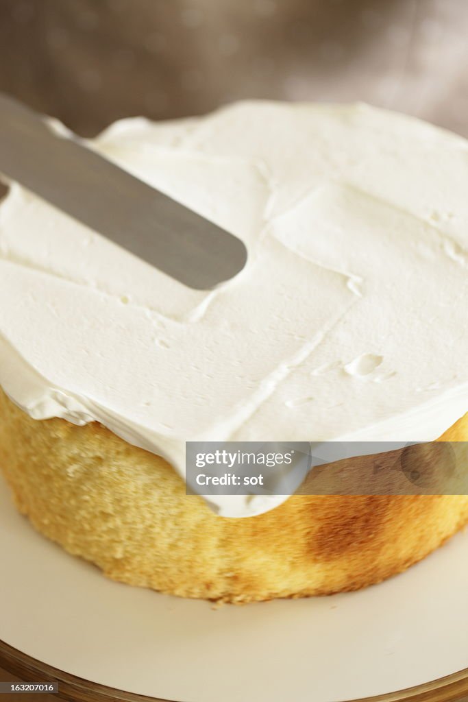 Woman spreading whipped cream on sponge cake