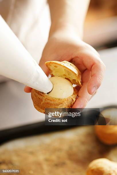 woman squeezing custard cream into cream puff - eclair stockfoto's en -beelden