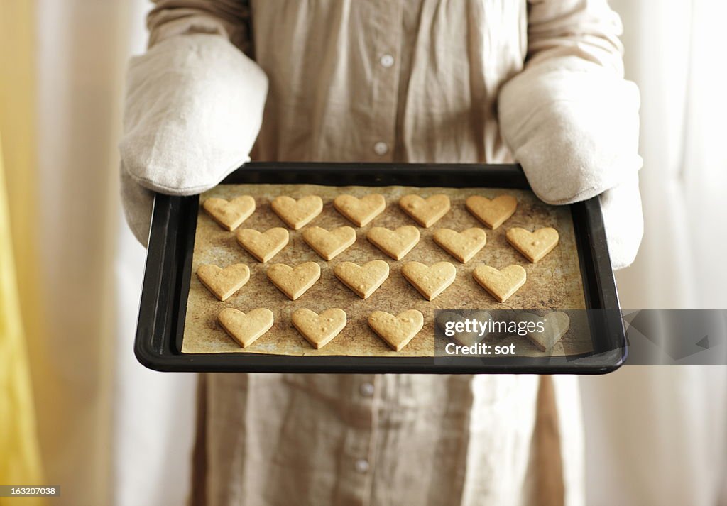 Woman holding oven tray of heart cookies