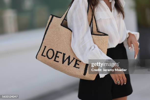 Milena Karl is seen wearing a white shirt with puffy sleeves, a large tote bag from Loewe in raffia, black shorts from Chloe, and gold and silver...