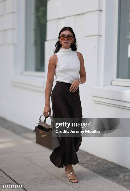 Milena Karl is seen wearing black sunglasses with orange lenses from Lexxola, golden earrings from Bottega Veneta, a creme-white sleeveless top from...