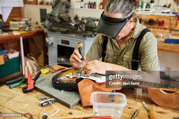 luthier man repairing an electric guitar with eye protection goggles in his workshop - instrument maker stock pictures, royalty-free photos & images