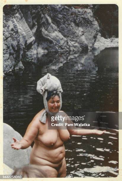 View of American educator Betty Fuller, naked with her clothes tied on top of her head, as she prepares to swim across Tassajara Creek during a hike,...