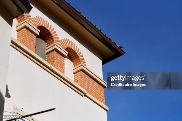 the upper part of a house, the corner, with several semi-circular windows with red bricks and high white walls, you can see the edge of the roof and the blue sky in the background. - private terrace balcony stock-fotos und bilder