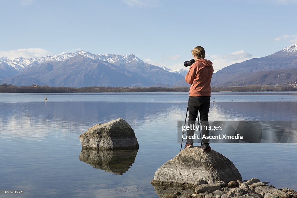 Young man takes picture from rock beside lakeshore