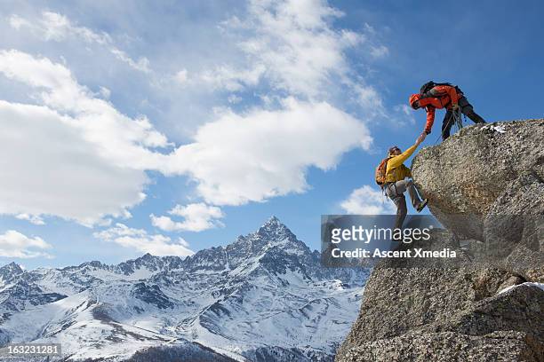 climber extends helping hand to teammate - climbing help stock-fotos und bilder