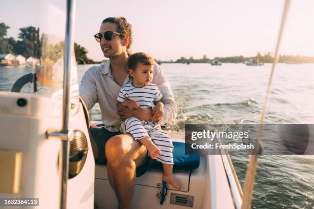 una linda niña seria mirando hacia otro lado mientras está sentada en un bote con su irreconocible padre - embarcación-marina fotografías e imágenes de stock
