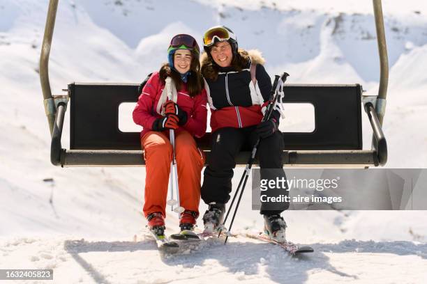 mother and daughter sitting on a ski lift on a ski slope, smiling looking at the bed, frontal view - woman on ski lift stock pictures, royalty-free photos & images