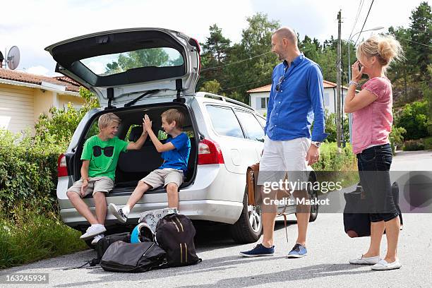 caucasian couple looking at happy sons sitting in car trunk before going for picnic - car picnic stock pictures, royalty-free photos & images