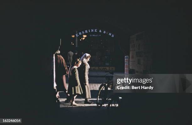 Pedestrians on a shopping street, seen through an archway, Belfast, Northern Ireland, June 1955. Original publication: Picture Post - 7825 - Belfast...