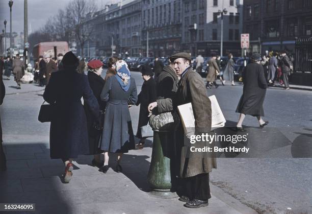 Newspaper vendor on a busy street in Dublin, Eire, June 1955. Original publication: Picture Post - 7808 - Dublin - pub. 18th June 1955.