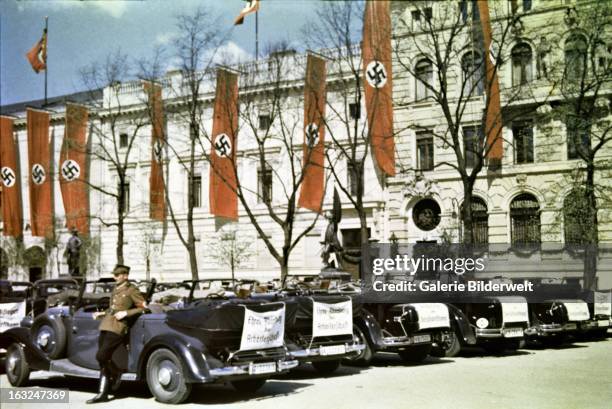 Driver leans against a state car smoking a cigarette. 1st May 1937. On the back of the car is a white cloth stating Ehren-Abordnung der...