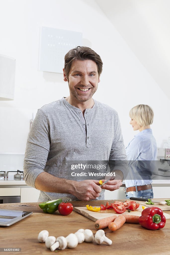 Germany, Bavaria, Munich, Mature man chopping vegetables, woman standing in background