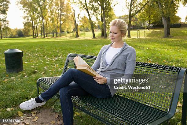 europe, germany, north rhine westphalia, duesseldorf, young woman reading book on park bench - mujer leyendo libro en el parque fotografías e imágenes de stock