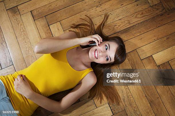 germany, berlin, young woman lying on floor and using smart phone - hände auf bauch stock-fotos und bilder