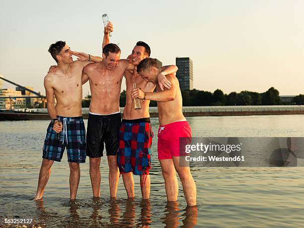 germany, duesseldorf, young friends drinking beer at riverbank - riverbank stock-fotos und bilder