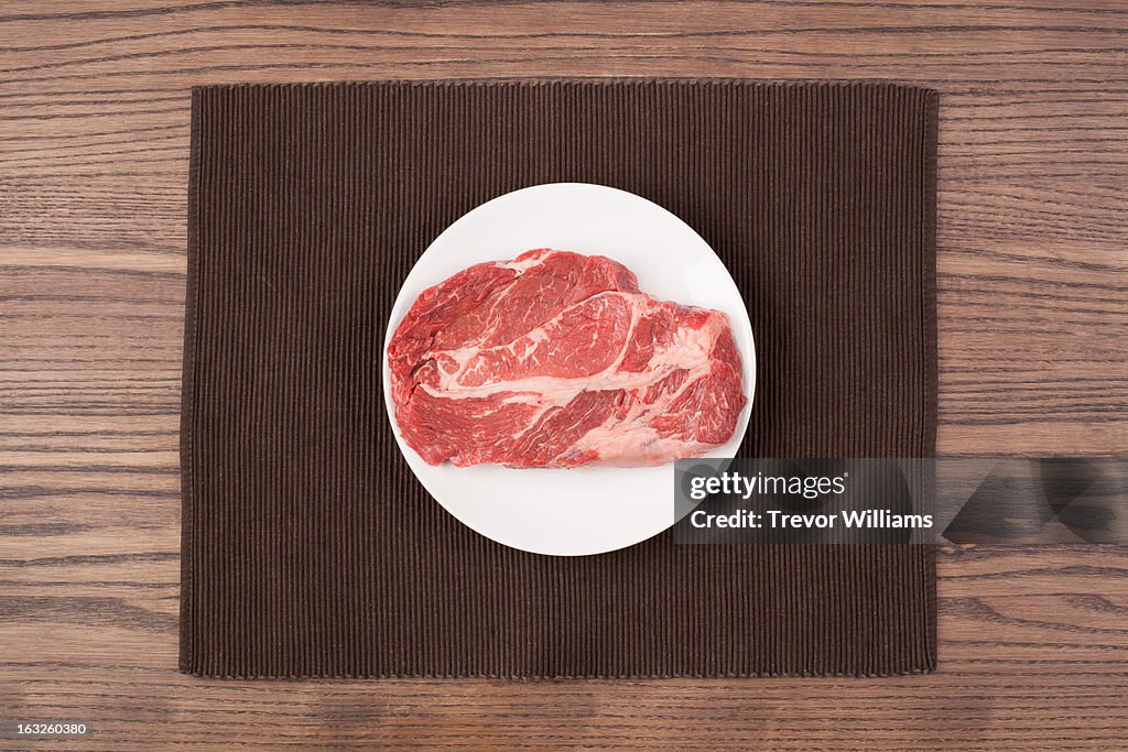 A raw steak on a plate on a wood table