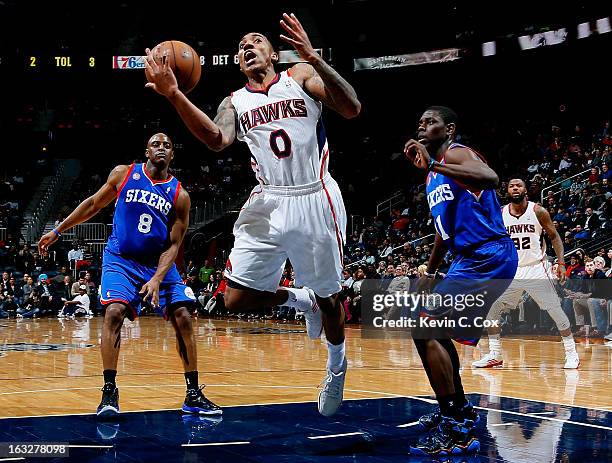 Jeff Teague of the Atlanta Hawks loses the ball as he drives between Damien Wilkins and Jrue Holiday of the Philadelphia 76ers at Philips Arena on...