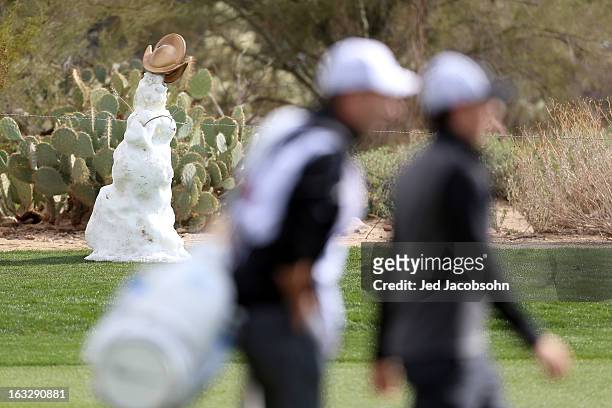 Rory McIlroy of Northern Ireland and his caddie JP Fitzgerald walk by a snowman on the second hole during the first round of the World Golf...