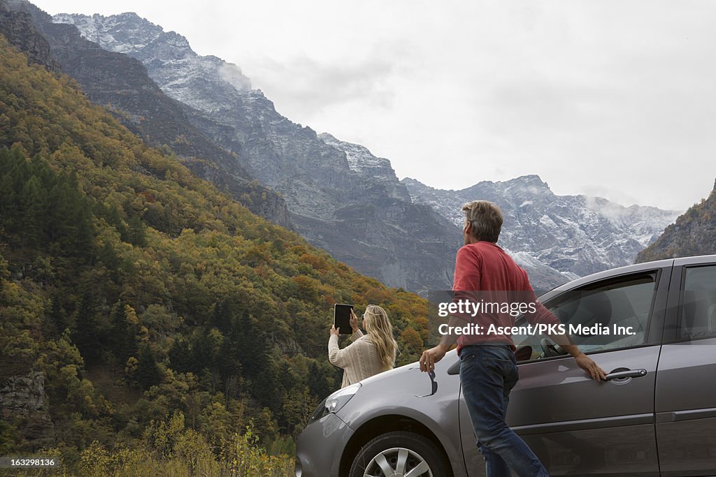 Couple take picture with tablet beside car in mtns
