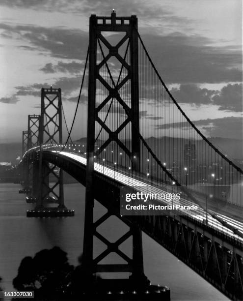 Straight view of the San Francisco-Oakland Bay Bridge in the evening with the lights on the bridge stretching for miles, California, 1955.