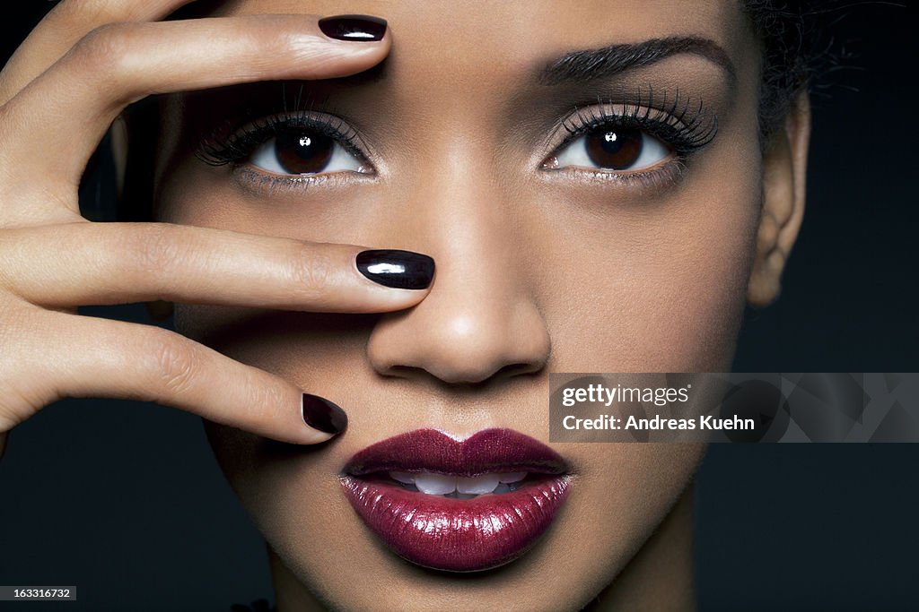 Young woman with red lips and black nail polish.