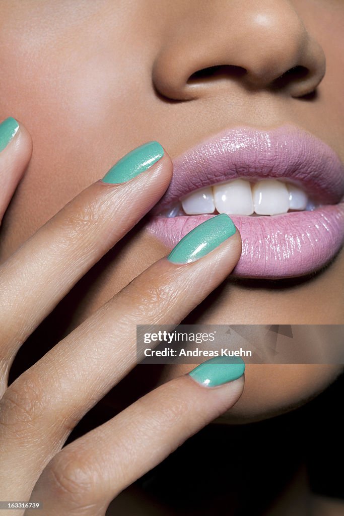 Young woman with teal colored nails and pink lips.
