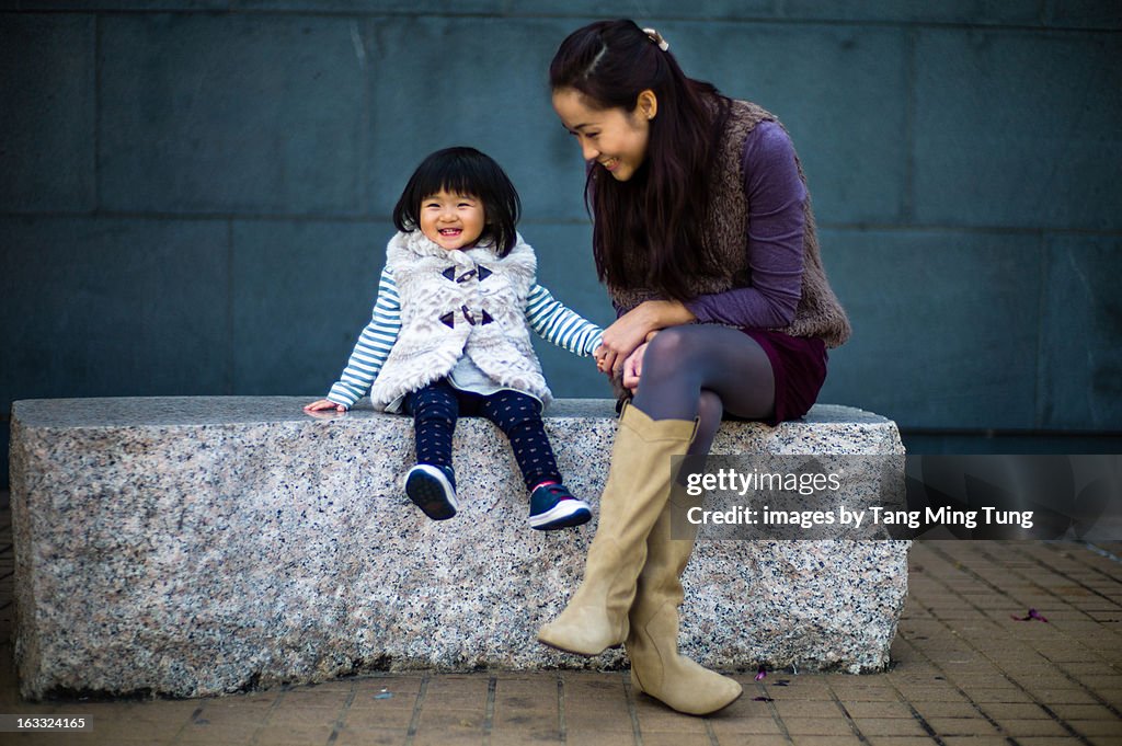 Pretty mom sitting with baby on bench joyfully.