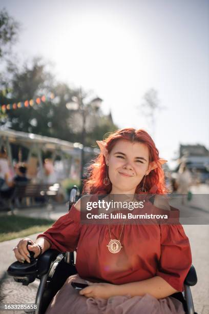 charming redhead woman in wheelchair dressed in cosplay outfit smirks at camera on sunny afternoon - cosplay stock pictures, royalty-free photos & images