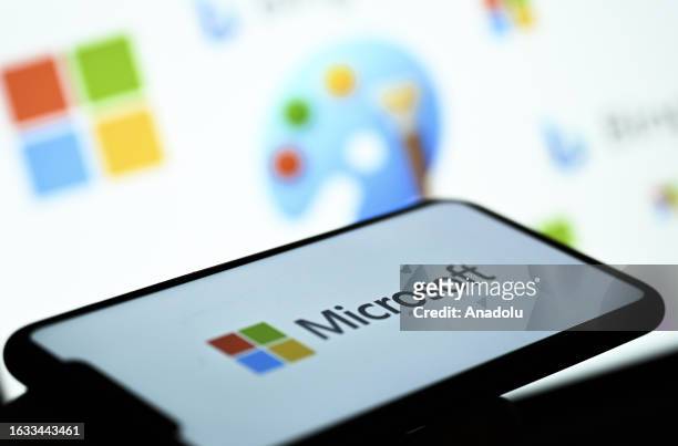 The logo of Microsoft is displayed on a mobile phone screen in front of a computer screen displaying the logos of Microsoft, Paint and Bing, in...