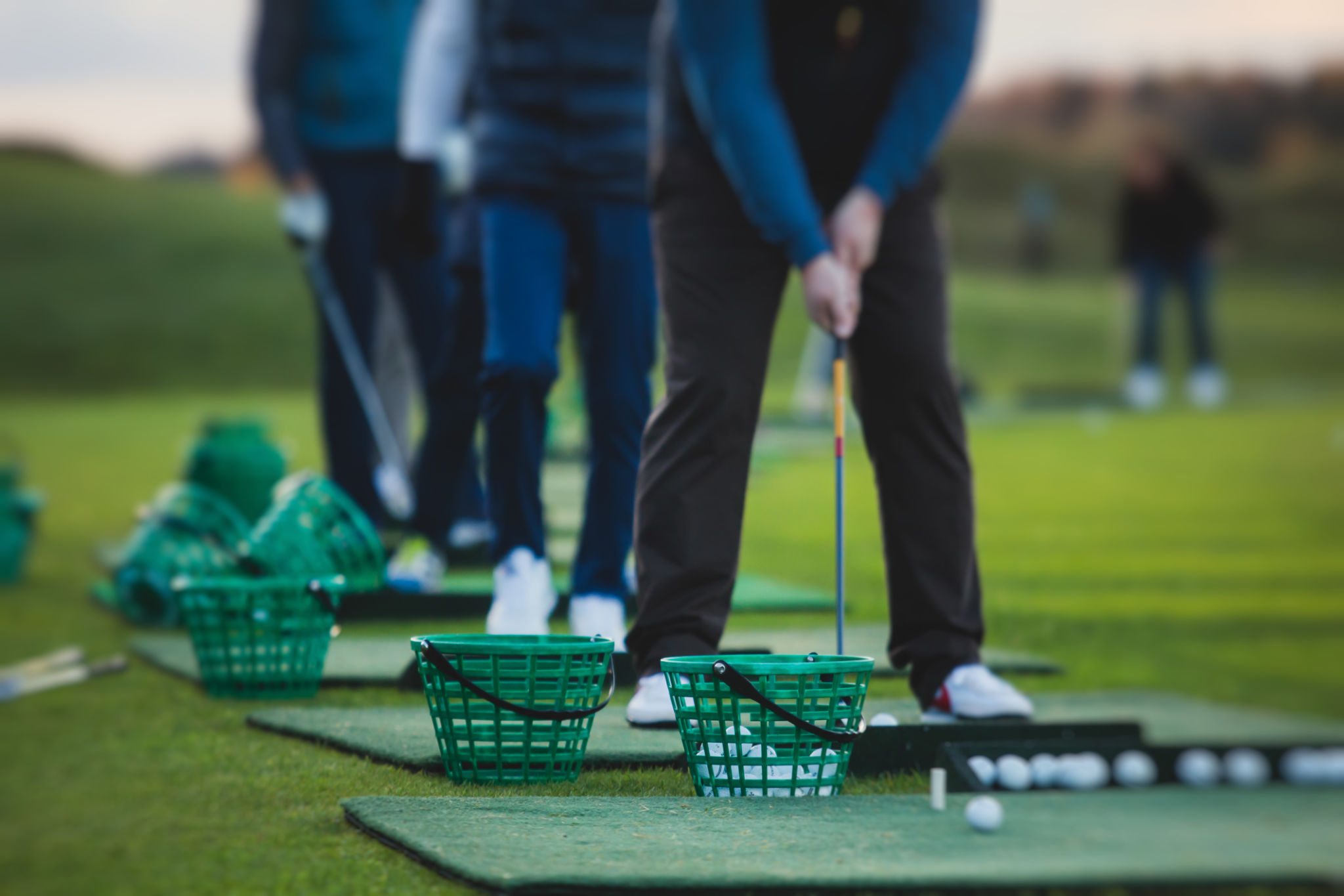 Group of golfers practicing and training golf swing on driving range practice, men playing on golf course, golf ball at golfing complex club resort Group of golfers practicing and training golf swing on driving range practice, men playing on golf course, golf ball at golfing complex club resort