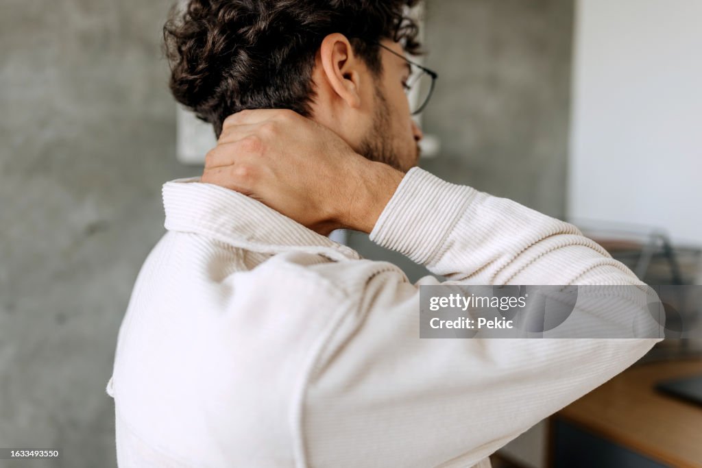 Close up shot of young man experiencing neck pain at home office
