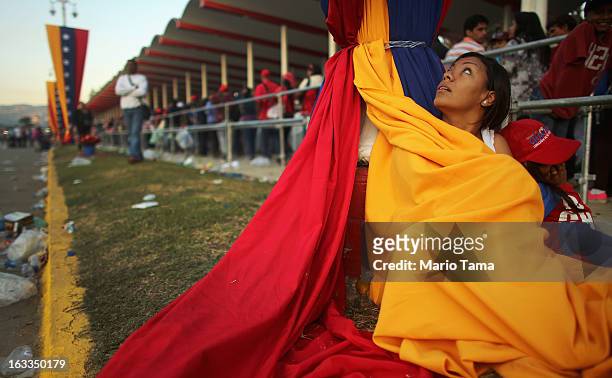 Woman keeps warm wrapped in the national flag as people wait in line before the start of the funeral for Venezuelan President Hugo Chavez outside the...