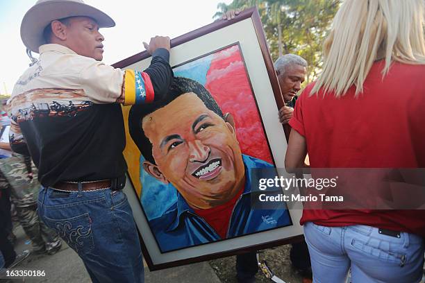 People carry a Chavez portrait before the start of the funeral for Venezuelan President Hugo Chavez outside the Military Academy on March 8, 2013 in...