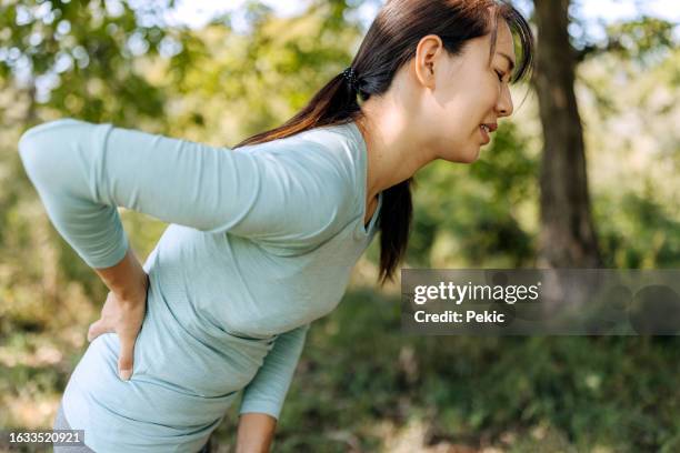 shot of a young woman experiencing back pain while working out in nature - indecisive woman stock pictures, royalty-free photos & images