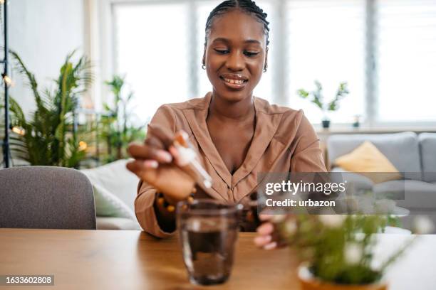 mujer joven poniendo gotas de medicina en un vaso de agua - homeopatía fotografías e imágenes de stock