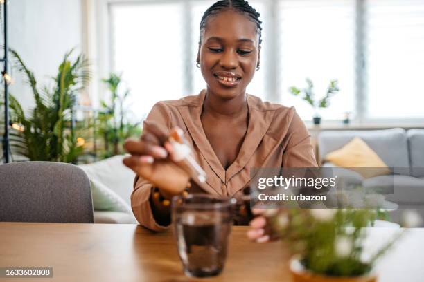 young woman putting medicine drops in a glass of water - homeopathic medicine stock pictures, royalty-free photos & images