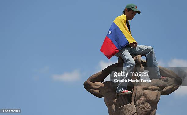 Young man wears a Venezuelan flag atop a statue outside the funeral for Venezuelan President Hugo Chavez at the Military Academy on March 8, 2013 in...