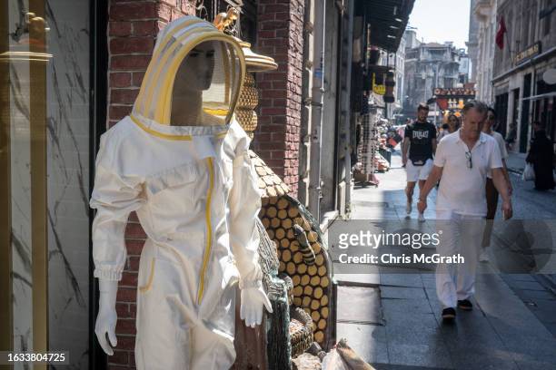 People walk on the street past a shop specialising in honey products and displaying a mannequin in a beekeepers outfit on August 23, 2023 in...