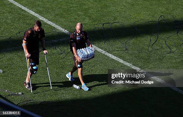 Matthew Suckling of the Hawthorn Hawks walks to the bus on crutches with fitness coach Andrew Russell after sustaining a right leg injury during the...